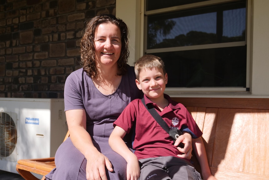 A woman with curly brown hair smiles, her young son has short brown hair and wears a red school uniform