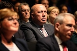 Peter Dutton sits in a crowd of Liberal members in a dark convention centre