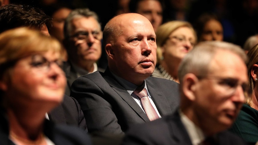 Peter Dutton sits in a crowd of Liberal members in a dark convention centre