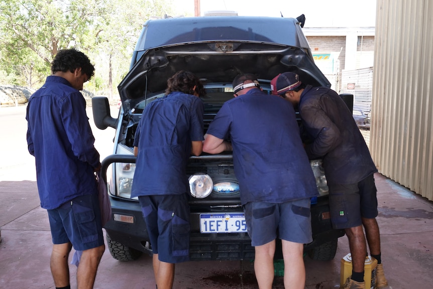 Four young mechanics pictured from behind working on a car