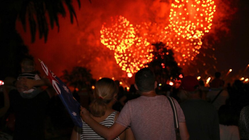 A man stands with his arm around a woman watching the Perth Skyworks, with bright orange fireworks exploding in the sky.