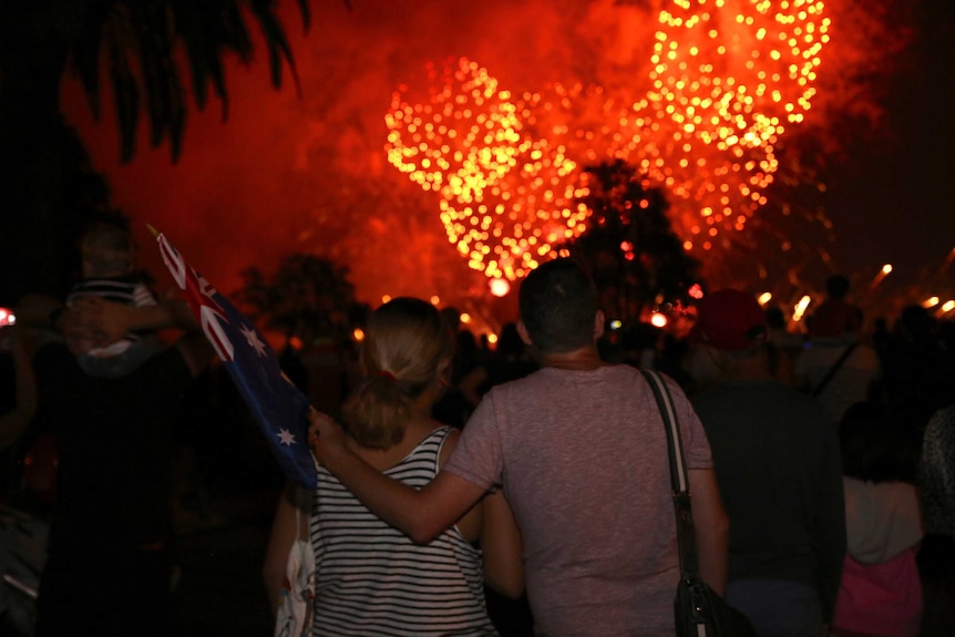 A man stands with his arm around a woman watching the Perth Skyworks, with bright orange fireworks exploding in the sky.