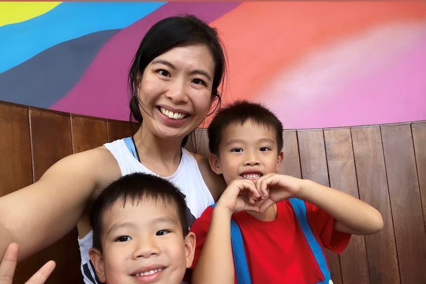 A Chinese woman smiles as she sits with two young boys in a colourful restaurant cubicle