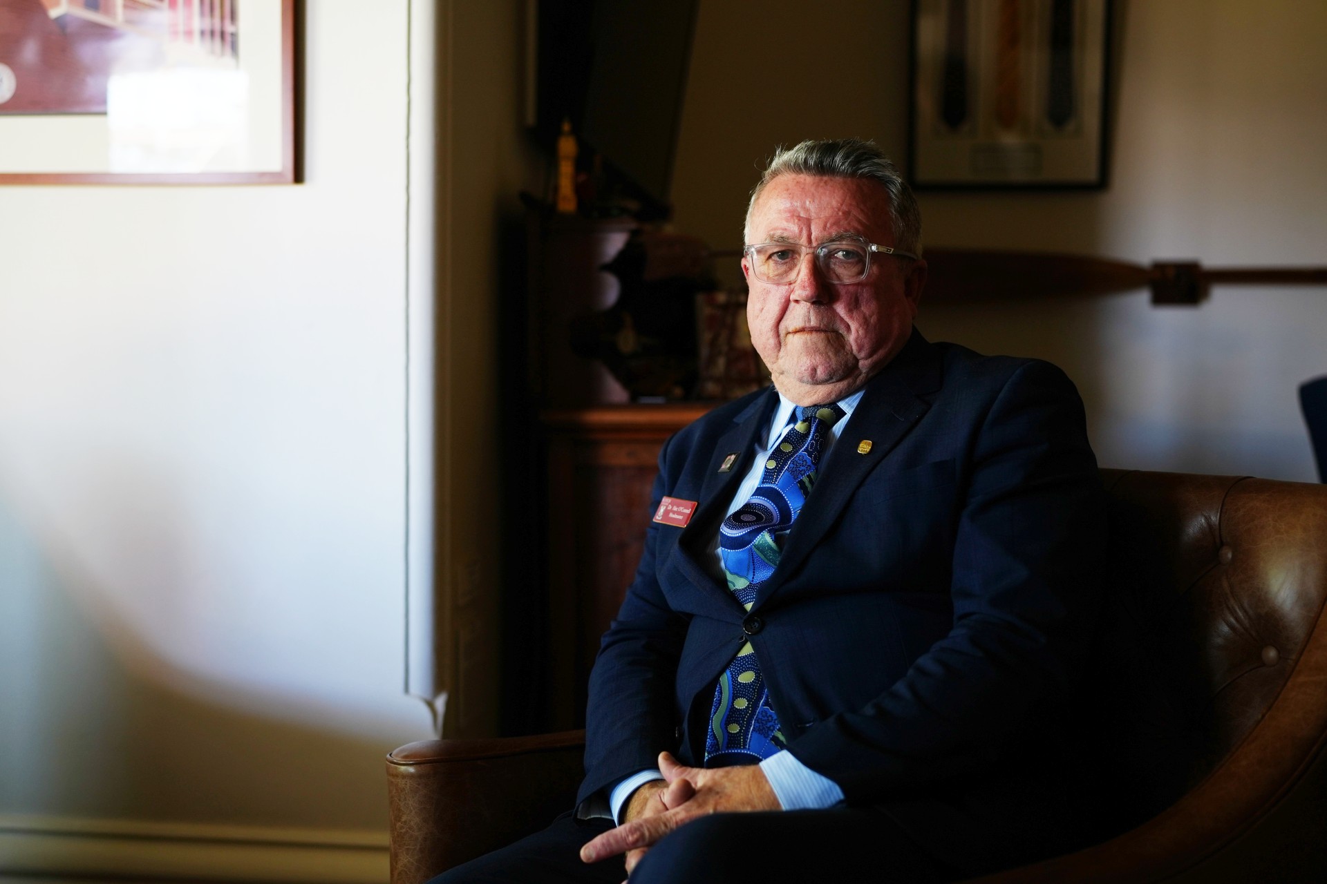 Alec wears a blue blazer and tie as he sits in his office