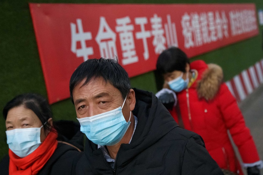 People wear face masks as they walk past a slogan at a Beijing construction site