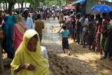 Refugees navigate a muddy path as others queue.