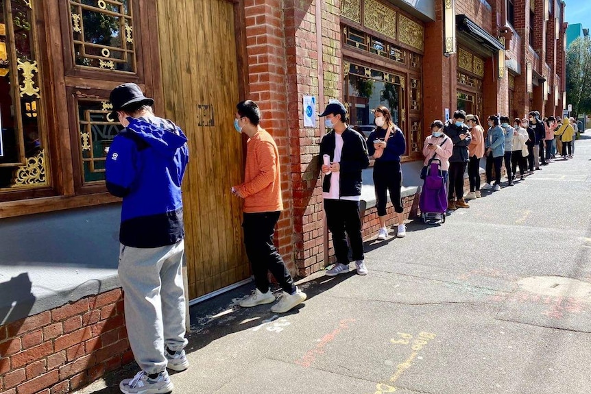 An ornate gold restaurant front, with a long line of about 20 people waiting for food, all distanced out.