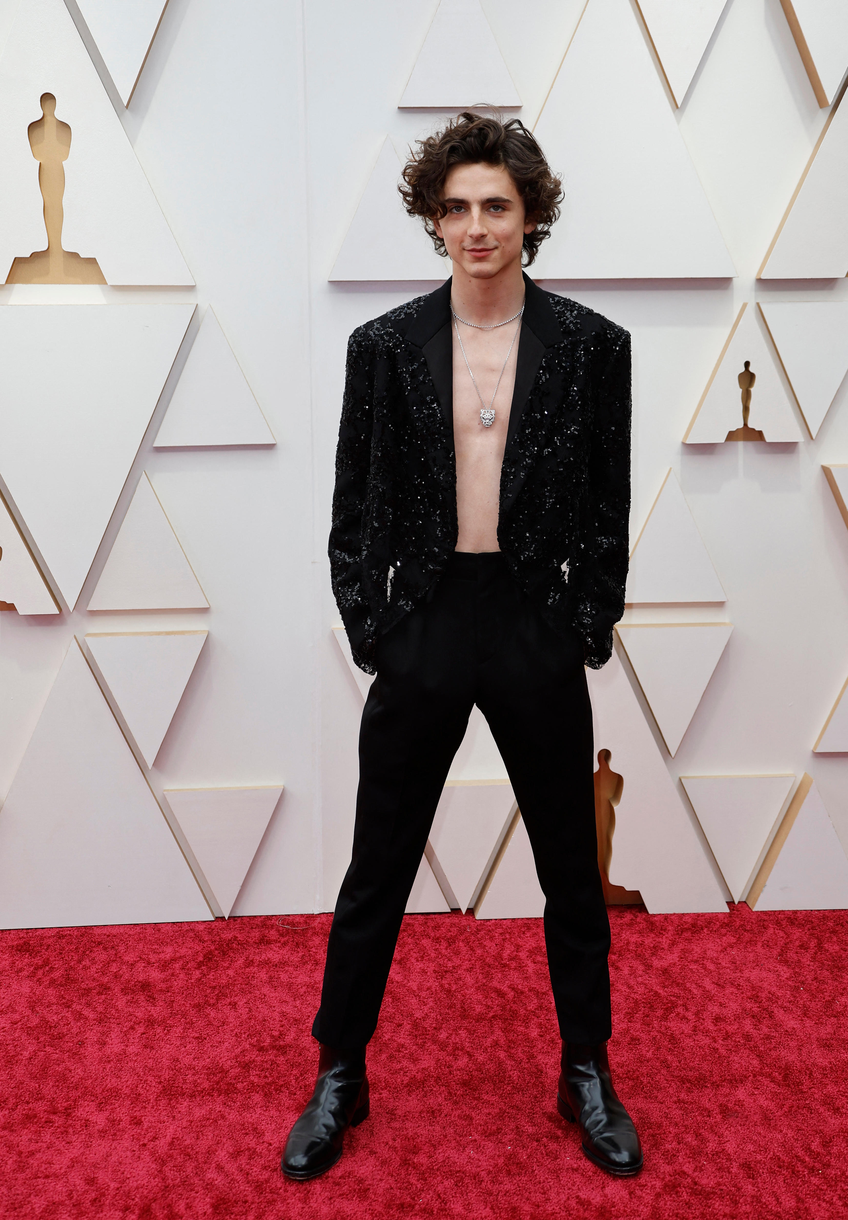 timothee chalamet stands on the red carpet wearing a sequinned black jacket, black pants and no shirt with a statement necklace