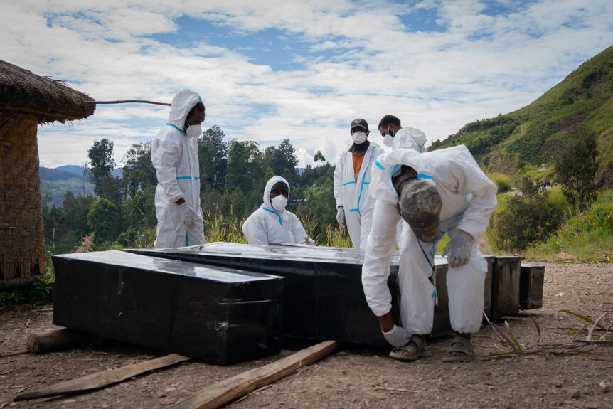 A group of men wearing hazmat suits standing around five black boxes.