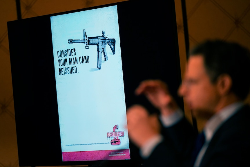 A screen in a courtroom shows an ad - a complex gun is shown next to the phrase 'consider your man card reissued'
