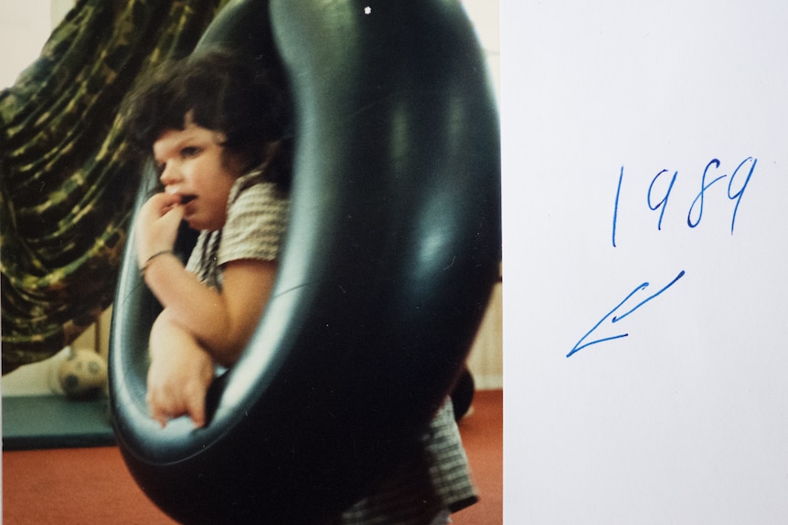 A young girl leans on a tyre swing.