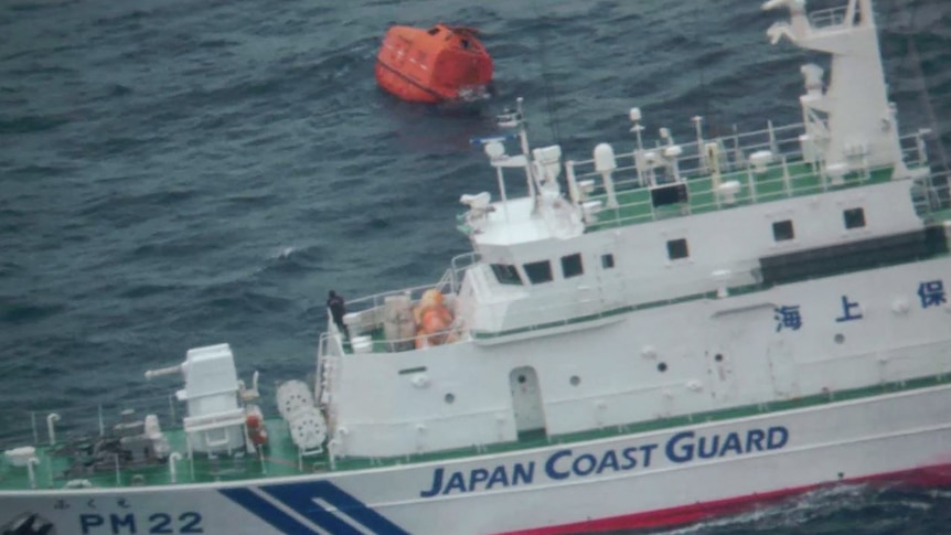 A Japan Coast Guard vessel at sea next to an orange lifeboat from the Jin Tian cargo ship