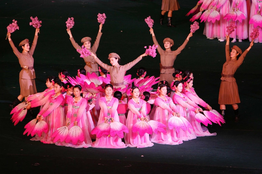 North Koreans don bright pink outfits like cherry blossoms and military uniforms as they perform on stage