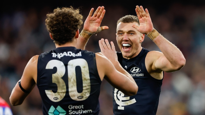 Carlton AFL captain Patrick Cripps grins as he prepares to clasp hands with a teammate (back turned to camera).