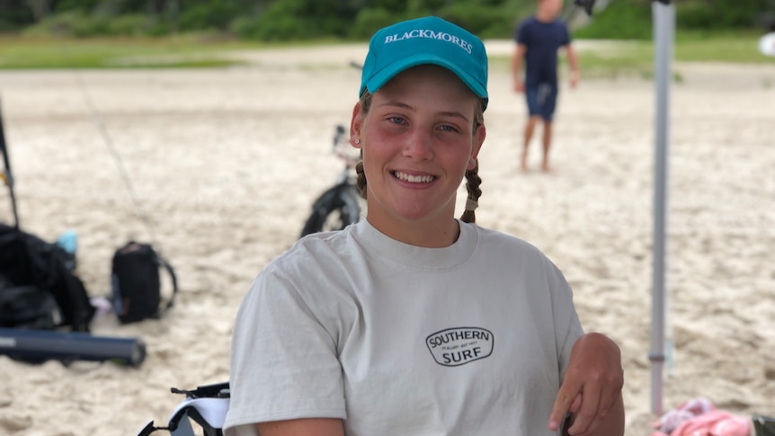 Young woman in a blue cap sits in a wheelchair on a beach