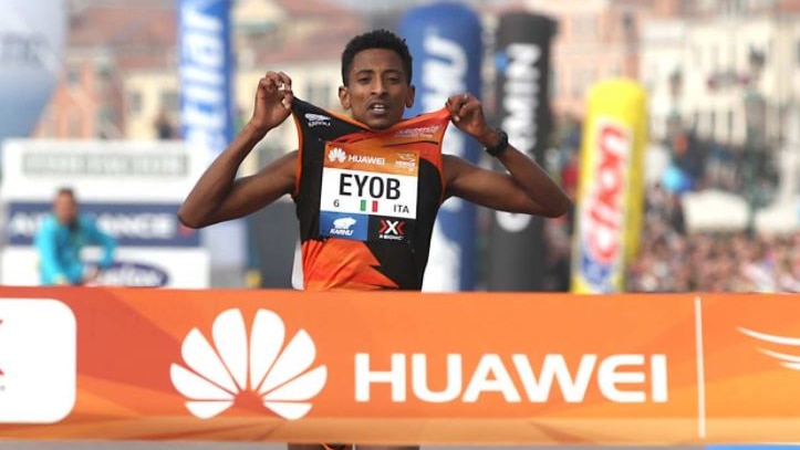 Eyob Faniel holds the shoulders of his singlet as he approaches an orange banner at the finish line of the Venice Marathon.