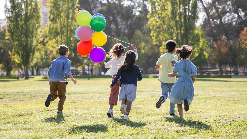 Children running in a park with a bunch of balloons