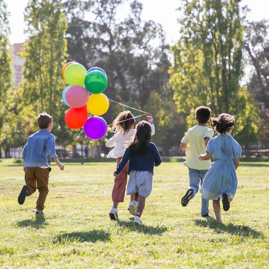 Children running in a park with a bunch of balloons