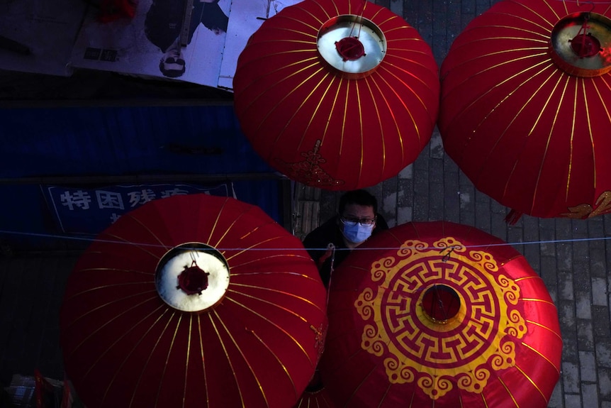 A vendor wearing a mask to protect from coronavirus uses a pole to lower lanterns