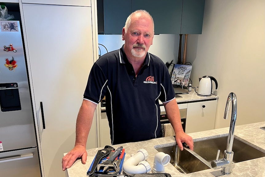 a man at a sink with tools on the kitchen bench