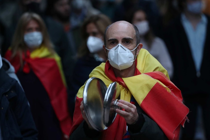 a man wearing the spanish flag wearing a face mask walks infront of a group of other people in masks