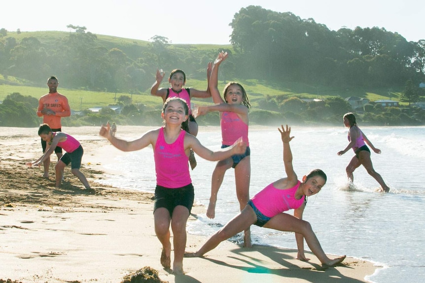 A group of young surf club kids showing off and jumping for joy on the beach