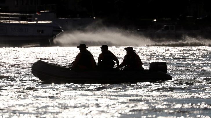 Three members of a South Korean rescue team are seen in silhouette no boat on glistening river.