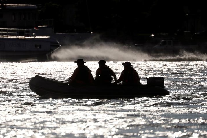 Three members of a South Korean rescue team are seen in silhouette no boat on glistening river.