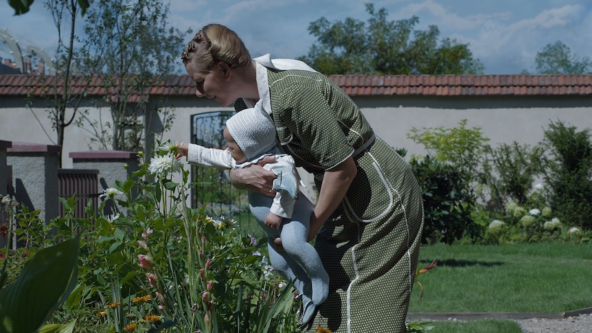 Sandra Huller in German braids holds a baby in a garden