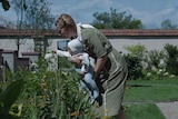 Sandra Huller in German braids holds a baby in a garden
