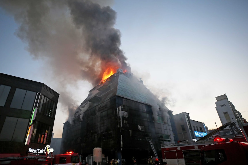 Smoke rises from a blaze at the top of an eight-storey building. Firefighters are at the scene.