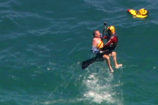 A man and his rescuer being winched above an ocean.