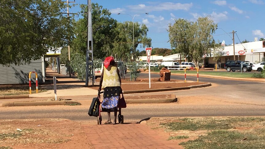 A woman with a red head scarf pushes a mobility walker along the street towards the shops