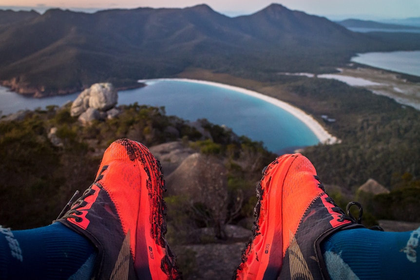Bright orange running shoes in the foreground, Wineglass Bay in the background.