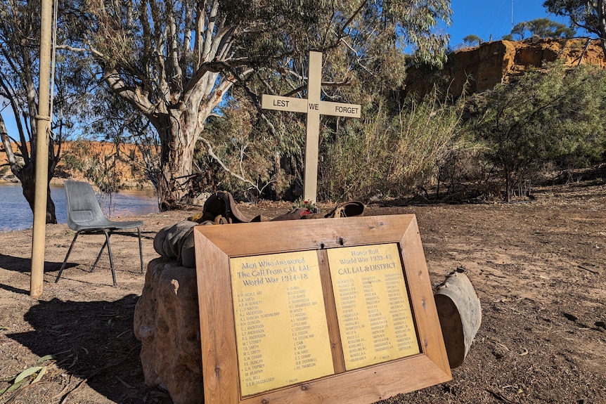 a lest we forget cross with an honour roll sitting on the dirt next to a river