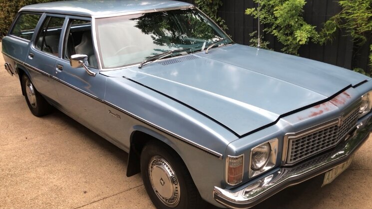A pale blue Kingswood station wagon is polished and parked in a driveway. 