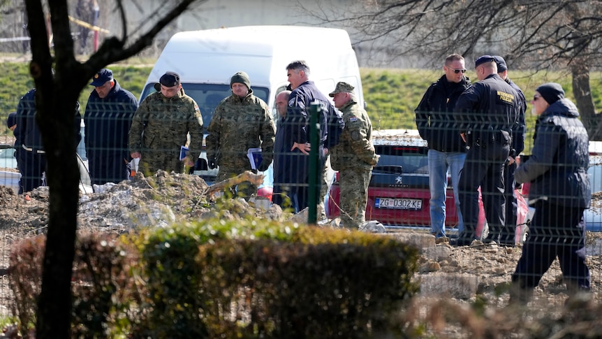 Police behind a fence inspect site of a drone crash.