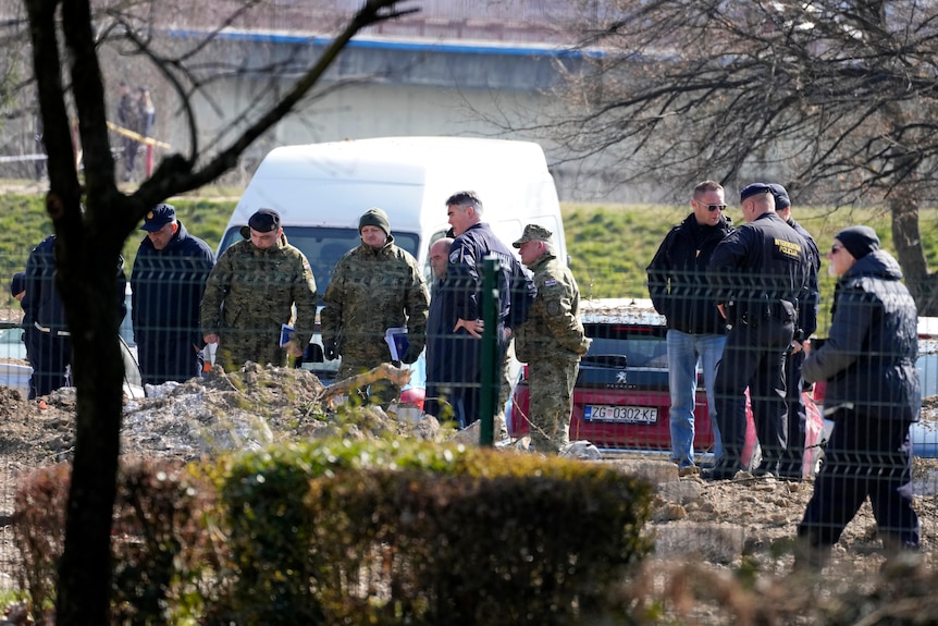 Police behind a fence inspect site of a drone crash.