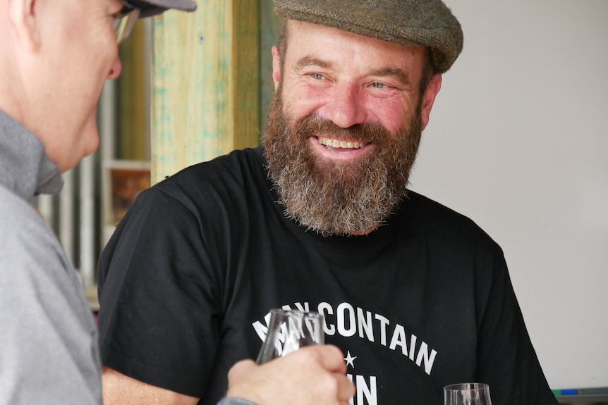 a man smiles at another drinking gin with a shirt reading ' may contain gin'