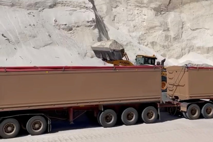 Ein Fahrzeug, das Kalksand in einen LKW transportiert, im Hintergrund viel Sand. 