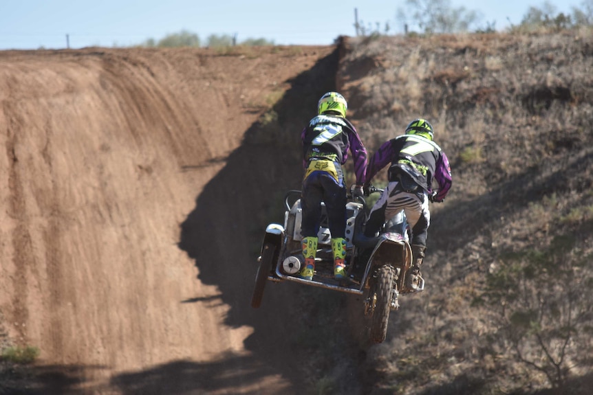 Two men on a motorbike and sidecar jump through the air in race gear.