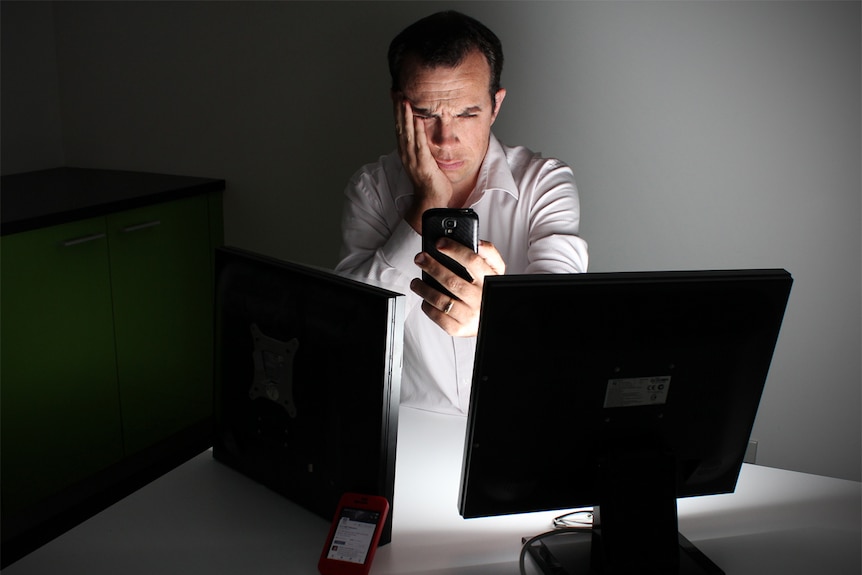 A man sits at a table surrounded by phones and screens.