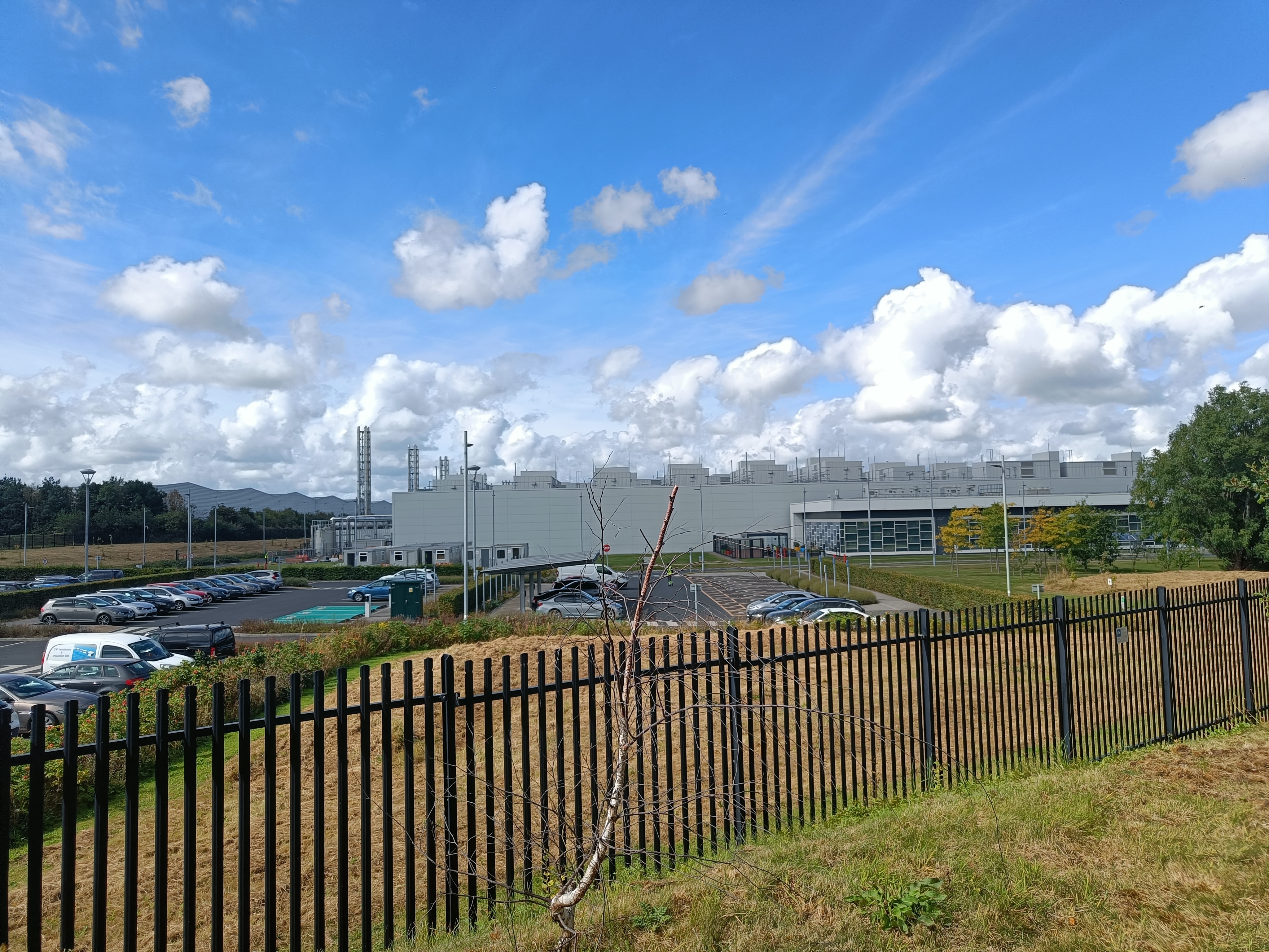 Black grated fence with factories in the distance.