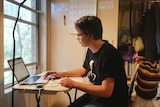 Zac Bonham sits at a desk and works on a laptop.