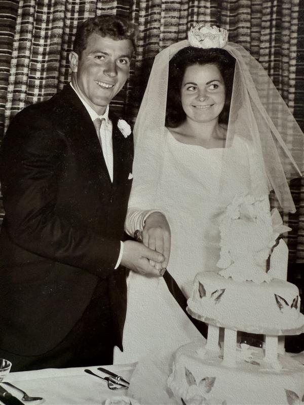 An old wedding photo of a bride and groom cutting their wedding cake smiling at the camera