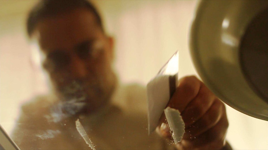 A man prepares lines of cocaine on a table.