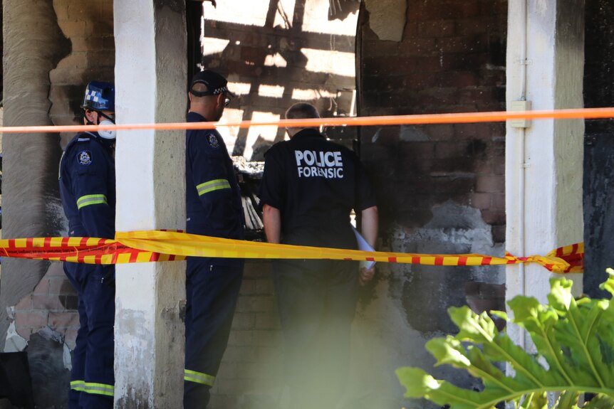 Police forensic officers look at a burnt house taped off