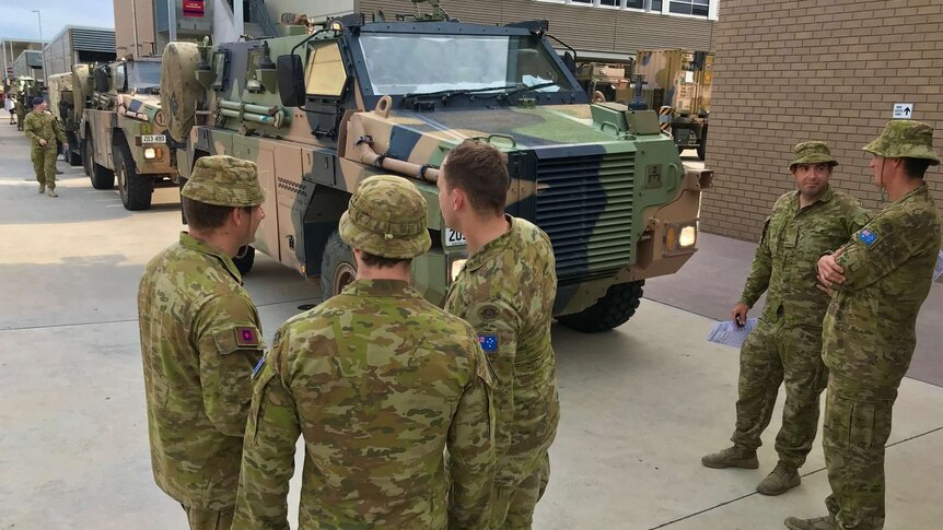 Soldiers dressed in fatigues standing alongside a camouflage transport vehicle