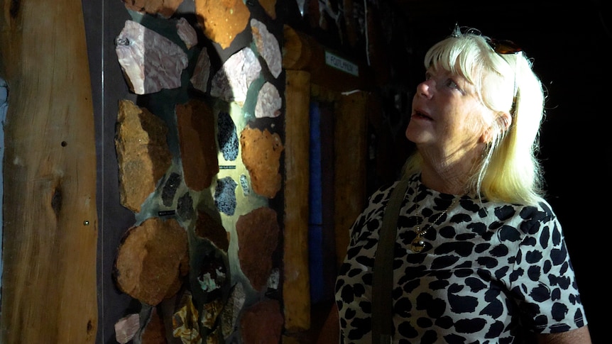 A woman in a dark room with rocks embedded in the walls, spotlit by light.