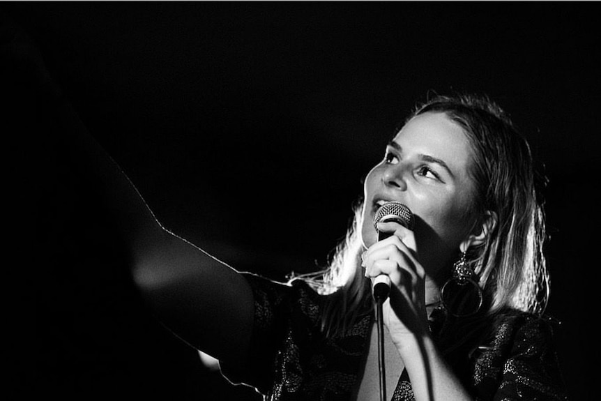 A black and white image of a woman singing into a mic
